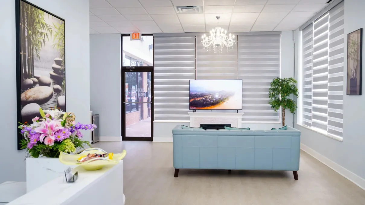 The reception lounge at May Breeze Spa in Livonia — seating, flowers and daylight through the front windows beneath a chandelier
