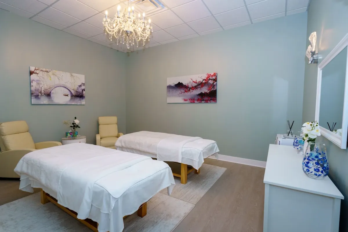 A treatment room at May Breeze Spa with two dressed massage beds and a chandelier